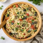 A large bowl of Best Italian Spaghetti Salad with fresh vegetables on a wooden table.