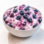 A creamy bowl of Blueberry Fluff Salad topped with fresh berries and marshmallows.