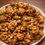 A plate of crispy Cashew Chicken with rice and green onions.