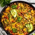 A cheesy Chicken Fajita Casserole with Rice in a cast iron skillet topped with peppers and cilantro.