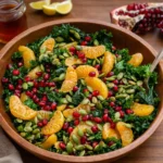 A vibrant Citrus Pomegranate Kale Salad in a wooden bowl.