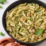 Bowl of Creamy Chicken Pesto Pasta with melted cheese and fresh basil.