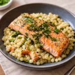 A plate of Herbed Pearl Couscous and Salmon with lemon wedges.