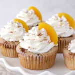 A close-up of Peach Cobbler Cupcakes with whipped cream and cinnamon.