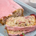 Freshly sliced Strawberry Banana Bread with pink glaze on a wooden board.