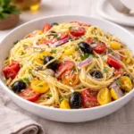 A vibrant bowl of California Veggie Spaghetti Salad on a wooden table.