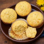 Golden brown dandelion muffins in a rustic basket with fresh flowers.